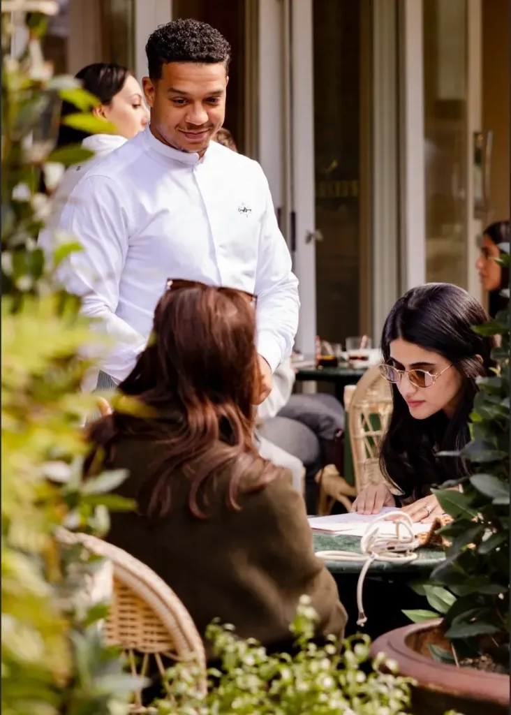A waiter in a white shirt attending guests at an outdoor London restaurant table